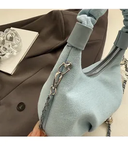 Close-up of a blue denim handbag with silver chain and pleated handle on a brown blazer