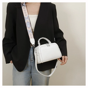 Close-up of white pebble leather Boston bag with silver studs and colorful woven strap