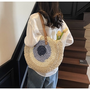 Detail of bohemian round straw bag with blue concentric circles and brown leather straps