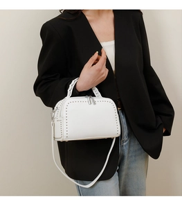 Detail of white litchi leather bag showing silver stud rivets and woven handle