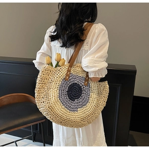 Detail of handwoven round straw tote bag with blue gradient pattern and leather straps