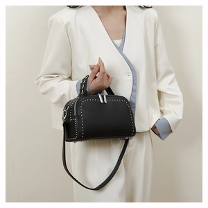 Detailed view of black pebbled leather handbag with silver rivets worn with white blazer
