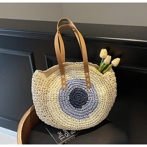 Detail of hand-woven straw tote bag with evil eye pattern and brown faux leather straps
