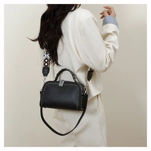 Detail of black pebbled leather handbag with silver rivets and woven shoulder strap
