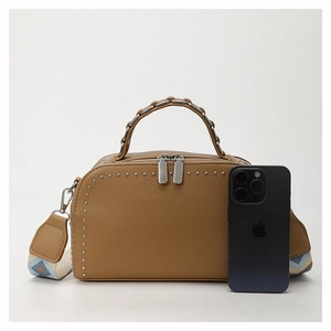 Detail of brown lychee texture bag with metal studs and geometric pattern strap
