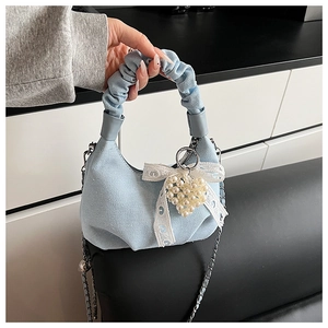 Detail of light blue denim bag featuring scrunchie handle, white lace bow, and pearl charm