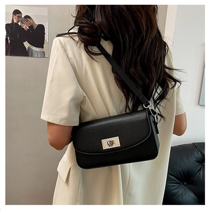 Detail of black lychee grain leather crossbody bag with silver turn-lock on female model
