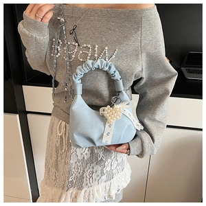 Detail of light blue denim handbag with ruched handle and pearl heart pendant