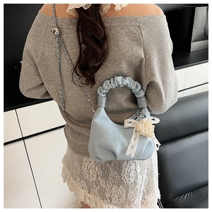 Detail of light blue denim pleated handbag with lace bow and pearl charm accents