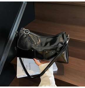 Dettaglio borsa a spalla in pelle verniciata nera con ciondolo a cuore e tasche con borchie