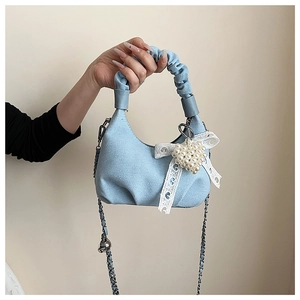 Detail of blue denim handbag featuring a white lace bow and large pearl heart charm