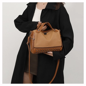 Detailed view of brown PU leather handbag featuring metal studs and side zipper accents