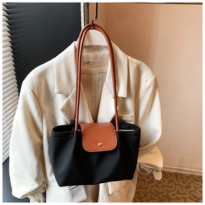 Detail of canvas tote bag featuring brown leather trim and golden metal snap button