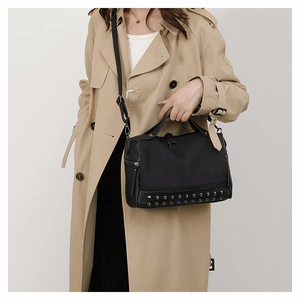 Detailed view of black PU leather handbag with silver rivets on beige trench coat