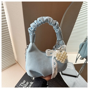 Detail of ruched handle on denim handbag with white lace bow and pearl heart charm