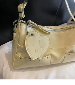Dettaglio della borsa tote in pelle PU giallo crema con ciondolo a cuore e rivetti