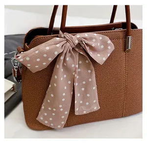 Gros plan d'un sac à main tissé marron orné d'un foulard en soie à pois roses