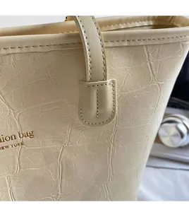 Detailansicht der beigen Tote Bag mit Krokodilprägung und goldener Logo-Prägung