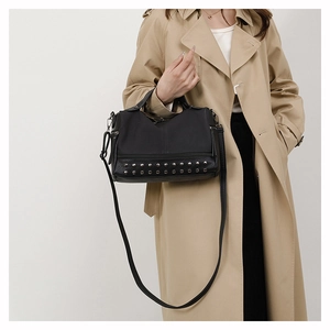 Detail of black PU leather handbag with silver rivets worn over a beige trench coat
