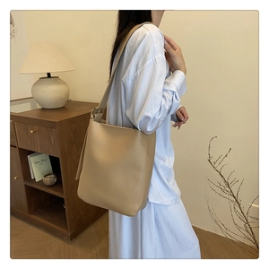 Detailed side view of a large beige tote bag worn by a model in a cozy minimalist room