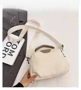 Detail of cream woven crossbody bag with brown leather handles and wide canvas strap