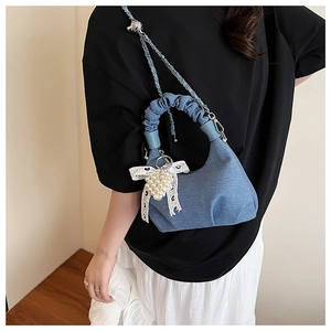 Detail of blue denim cloud bag with lace bows, pearls, and a silver chain strap