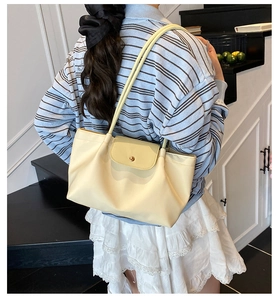 Detail view of cream-colored shoulder tote bag with gold button and soft pleated texture