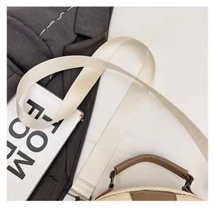 Detail of wide cream woven strap and brown leather handle on a stylish handbag