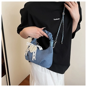 Detail of blue denim cloud bag with soft pleated handle and pearl lace bow charm