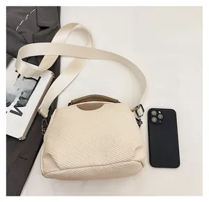 Detailed view of beige woven handbag with brown handle and strap next to a smartphone