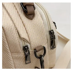 Detail view of the smooth dual metal zippers on a beige textured woven shoulder bag