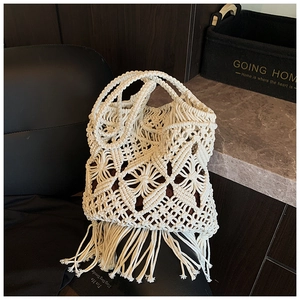 Détails du motif géométrique ajouré et pompons bohèmes sur le sac en paille crème