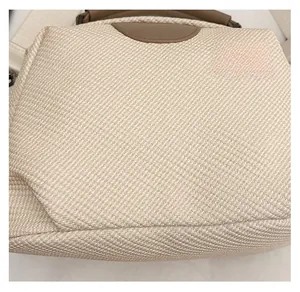 Detail of woven fabric texture with brown leather accents on a beige shoulder bag