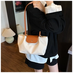 Detail of a minimalist off-white nylon tote bag with brown leather flap and golden snap