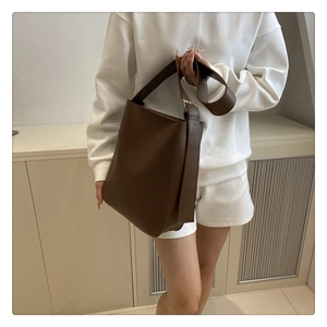 Detail of dark brown leather bucket bag showing adjustable wide strap and polished metal buckle