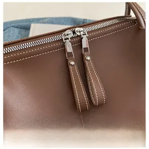 Detail of dual silver zippers with brown leather pullers and white contrast stitching