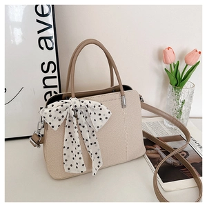 Détail du sac bandoulière tissé beige clair avec nœud à pois et anses marron