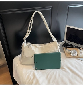 Borsa a spalla bianco crema con pendente a cuore e borchie accanto a un tablet per scala