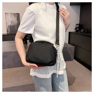 Close-up of black textured crossbody bag with ribbed fabric and wide woven shoulder strap