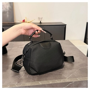 Detail of black crossbody shell bag with textured fabric and leather top handle