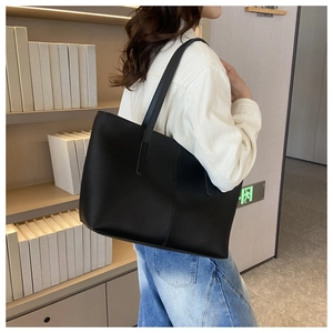 Model wearing a large black minimalist leather tote bag in a library setting with bookshelves