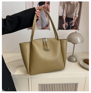 Detailed view of olive green leather tote bag with long zipper pulls on a modern display
