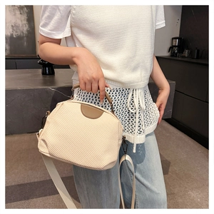 Detail of cream woven crossbody bag with brown leather handles and adjustable fabric strap