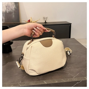 Detail of off-white woven handbag with brown leather handles and adjustable wide strap