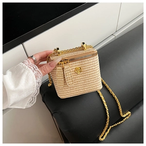 Detail of woven straw mini box bag with golden rose metal emblem and chain strap