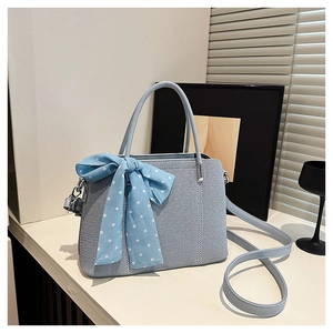 Détail d'un sac à main bleu clair avec texture tressée, foulard à pois et bandoulière