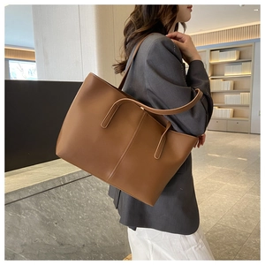 Close-up of caramel brown leather tote bag worn by model in a modern interior setting
