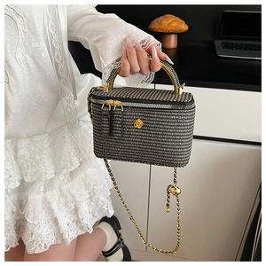 Detail of black and white woven mini box bag with gold floral clasp and chain strap