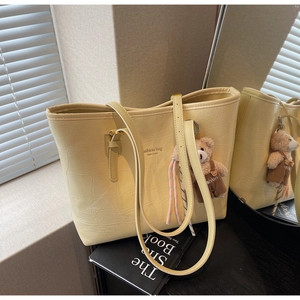 Detail der beige Tote Bag mit Krokodilmuster, Bärenanhänger und geflochtener Kordel