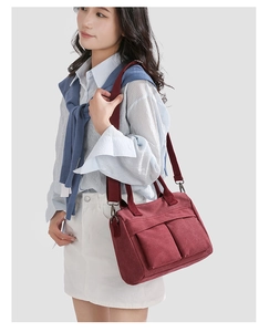 Deep red canvas tote bag with dual front pockets and adjustable strap shown on model
